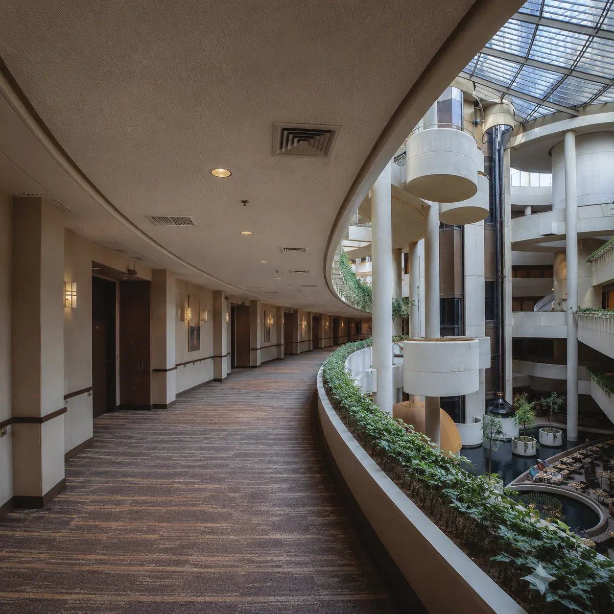 Existing atrium corridor — a generous void with real architectural quality, but mechanical ducting dominates, planting is token, and the space relies entirely on artificial climate control.